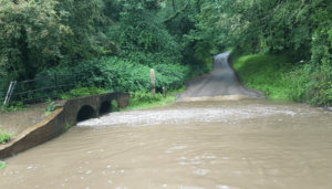Image of the Stour at Traitor's Ford in flood. The classic double tunnel foot bridge is at the left. The water has half filled the tunnels.